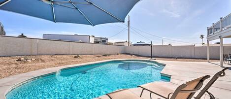A swimming pool with lounge chairs and an umbrella.