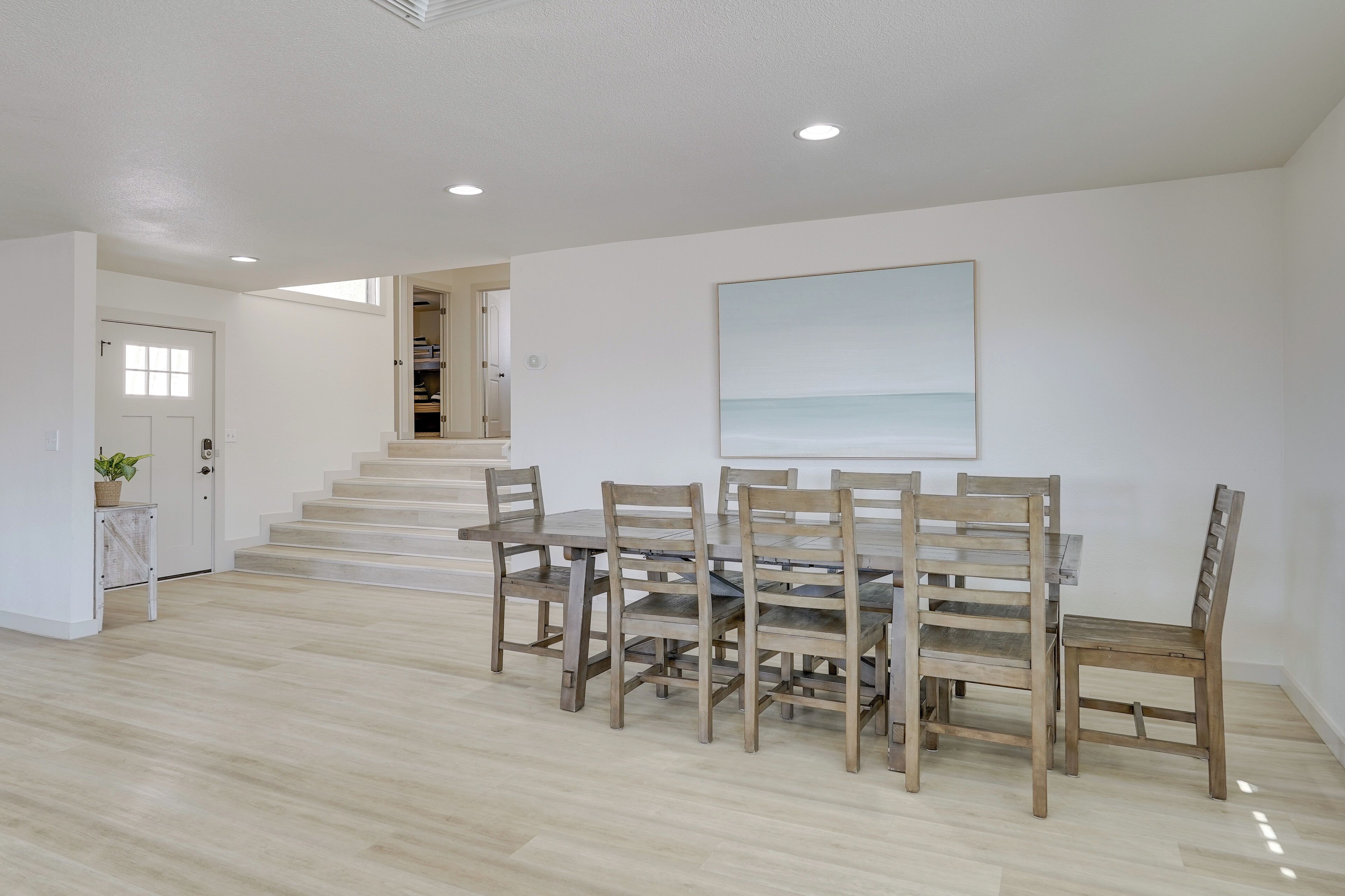 A dining area with a wooden table and chairs, a staircase leading to another room, and a painting on the wall.