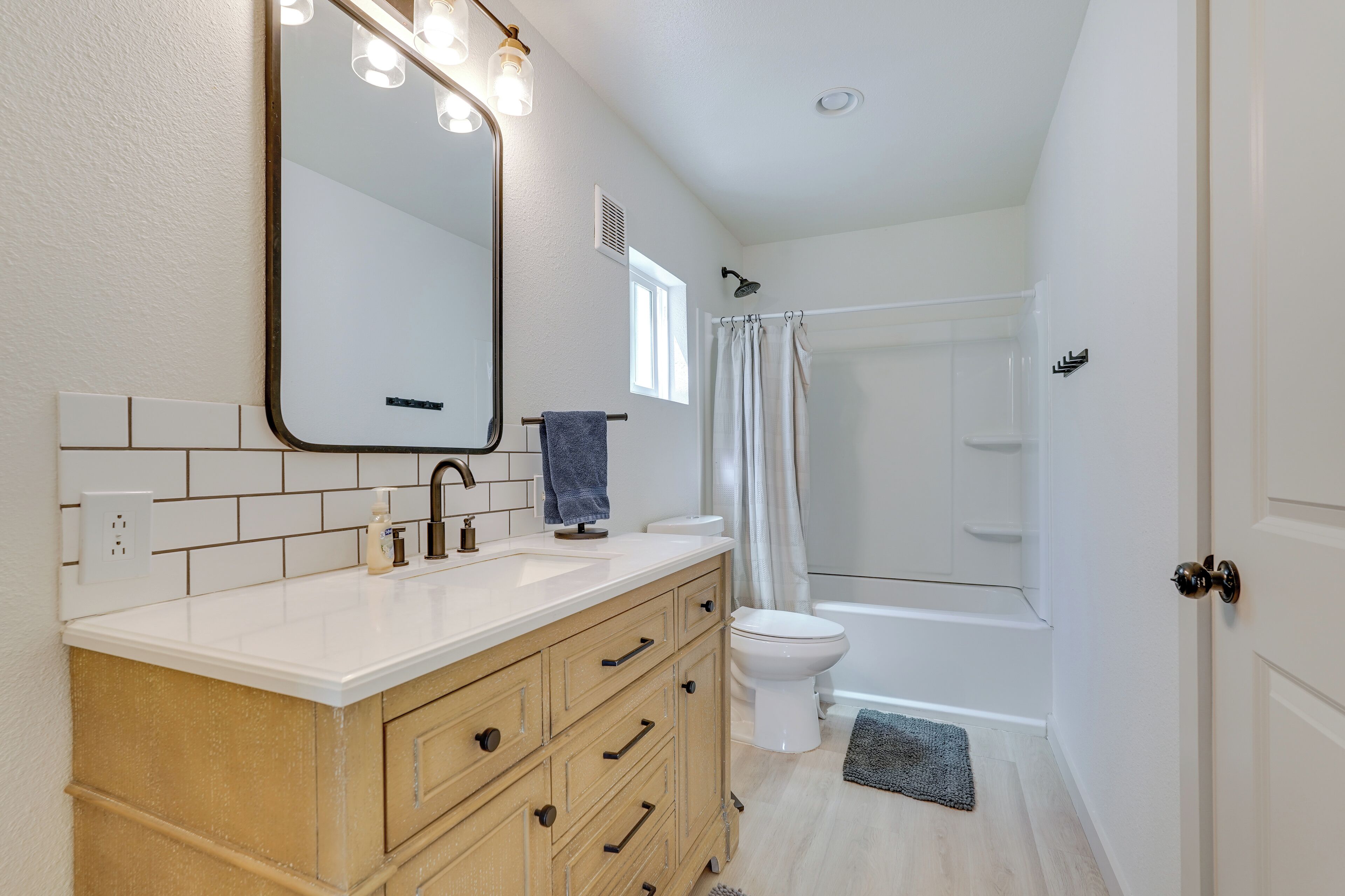 Une salle de bain avec un lavabo blanc, un meuble-lavabo en bois, un grand miroir, une douche et des toilettes.