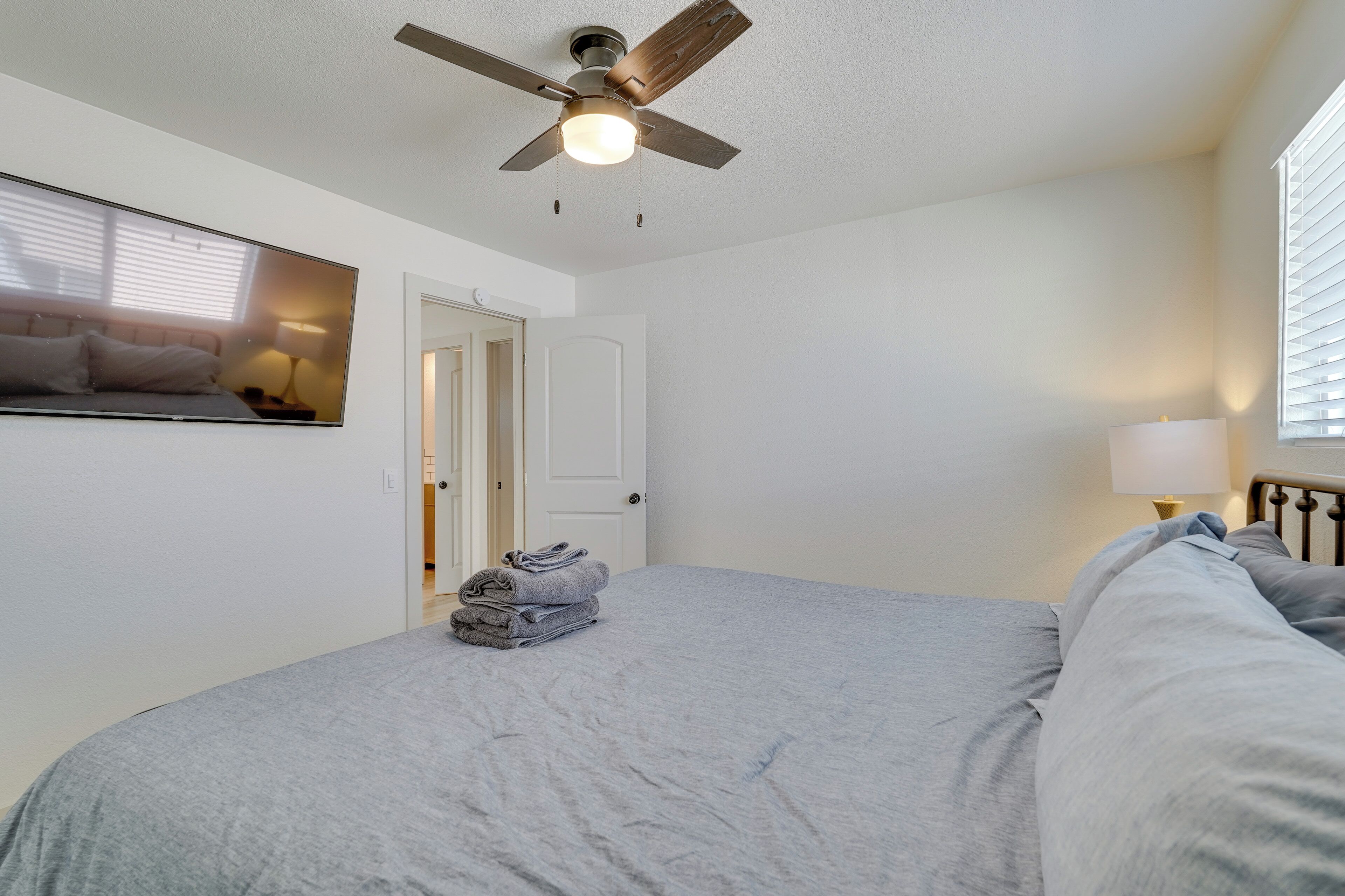 A bedroom with a bed, a ceiling fan, a door, and a window with blinds.