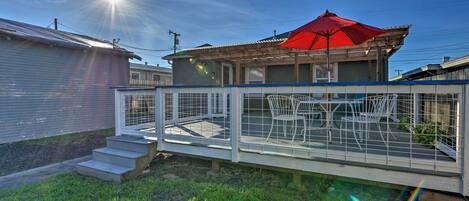 A house with a red umbrella, a fenced patio with chairs, and a clear sky.