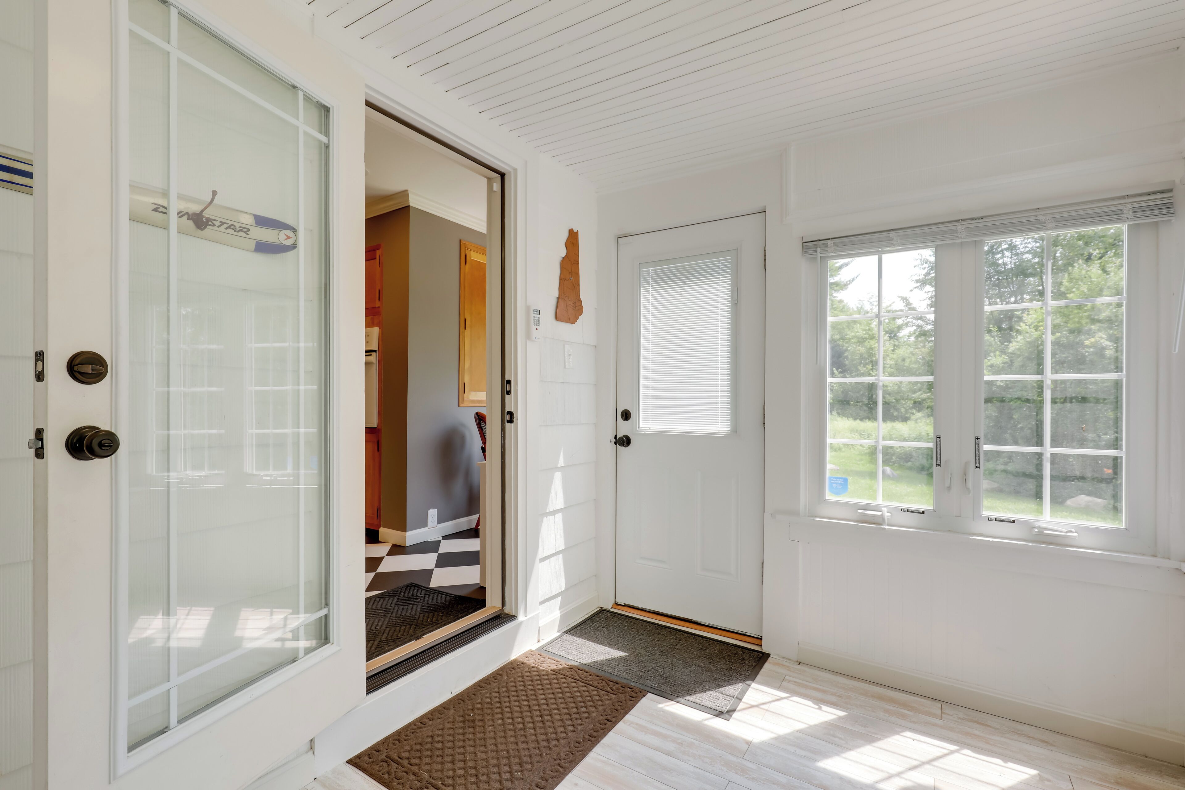 A clean, well-lit entryway with a glass door, a wooden floor, and a window with blinds.