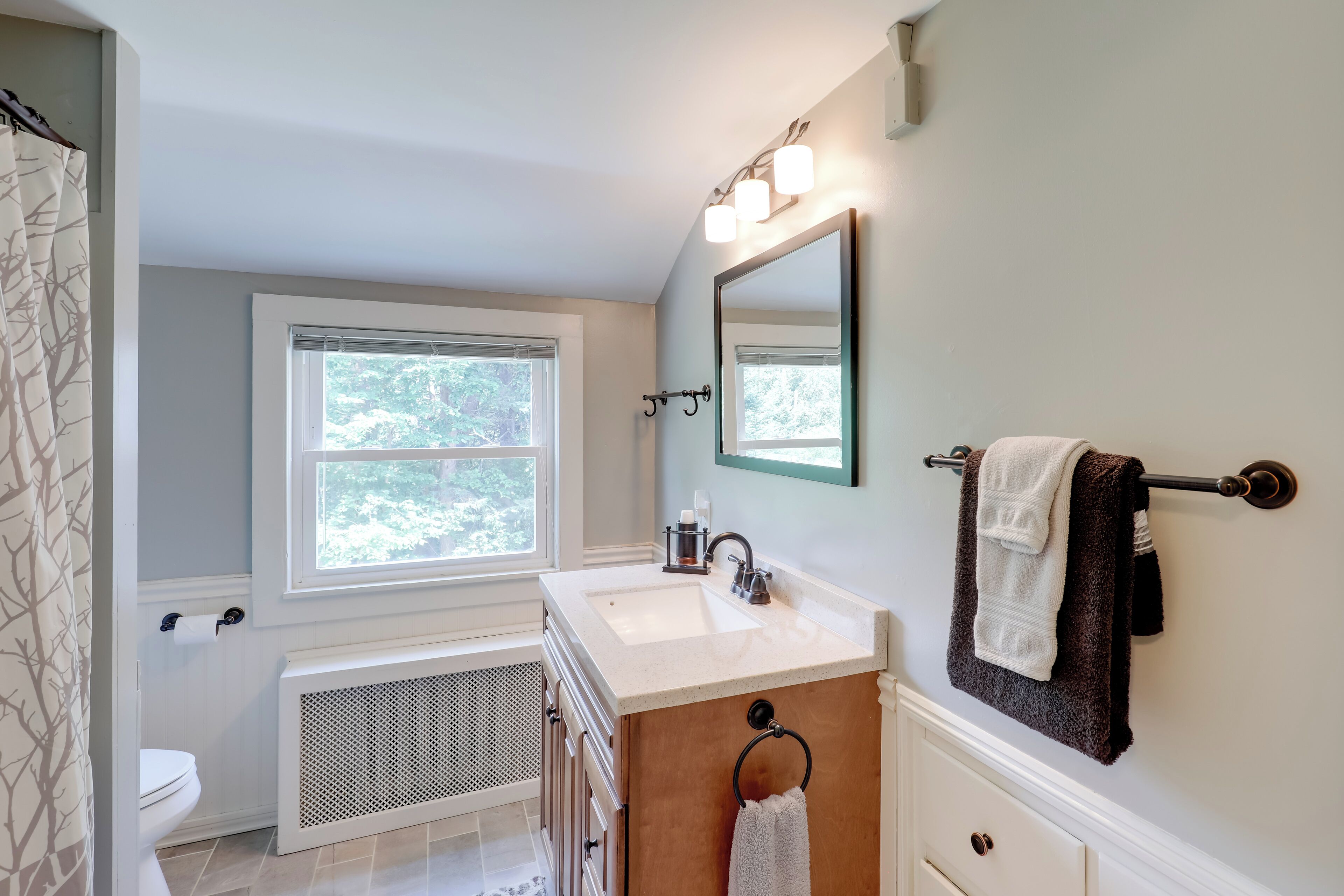 A bathroom with a white sink, a mirror, a towel rack, and a window.