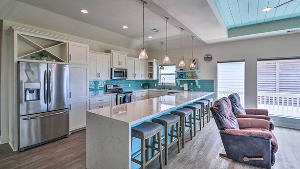 A modern kitchen with a central island, stainless steel appliances, pendant lighting, and a seating area with cushioned chairs. - Walk to Ocean: Bright Crystal Beach House w/ Deck! (Port Bolivar)