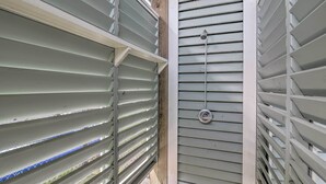 A narrow hallway with metal blinds and a door with a showerhead. - Walk to Ocean: Bright Crystal Beach House w/ Deck! (Port Bolivar)