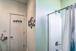 A bathroom with a white door, a towel hanging on the door, a shower curtain, and a showerhead.