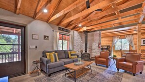 A cozy living room with a stone fireplace, wooden beams, a sofa, and leather chairs. - Cabin in Tonto National Forest: Deck & Views! (Pine)