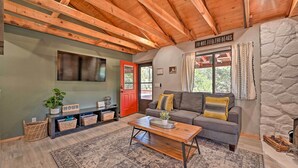A cozy living room with a wooden ceiling, a gray sofa, a coffee table, and a red door. - Cabin in Tonto National Forest: Deck & Views! (Pine)