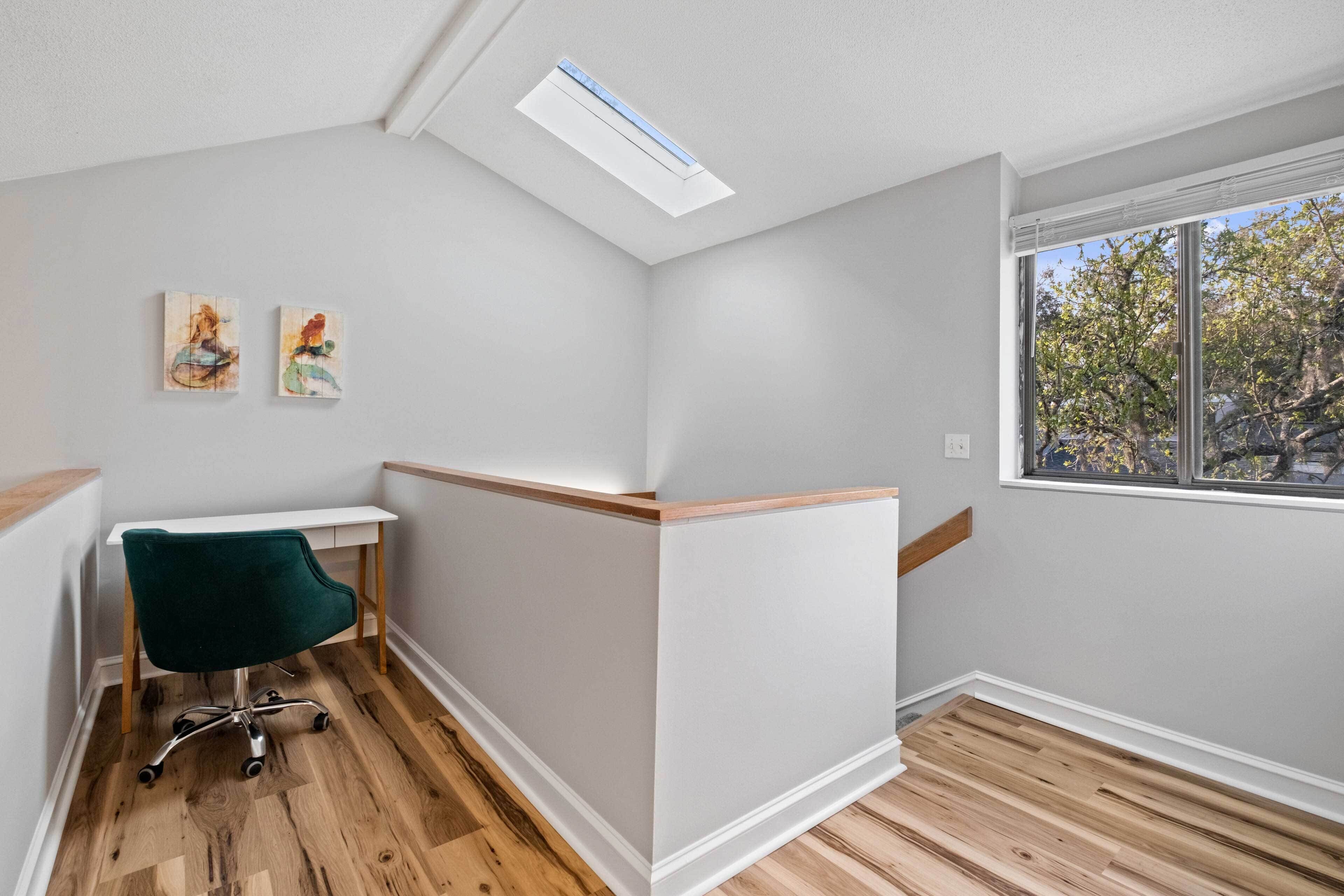 A corner room with a skylight, a desk, a chair, and two paintings on the wall.