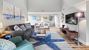 A modern living room with a sofa, coffee table, and TV. There are paintings on the wall and a star-patterned rug. - Walk to Coligny Beach Park: Coastal Oasis w/ Pool (Hilton Head Island)