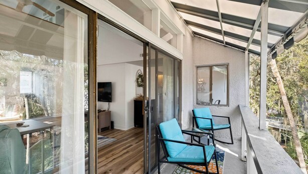 A modern living room with a glass door leading to a balcony, a flat-screen TV, and two blue chairs. - Walk to Coligny Beach Park: Coastal Oasis w/ Pool (Hilton Head Island)