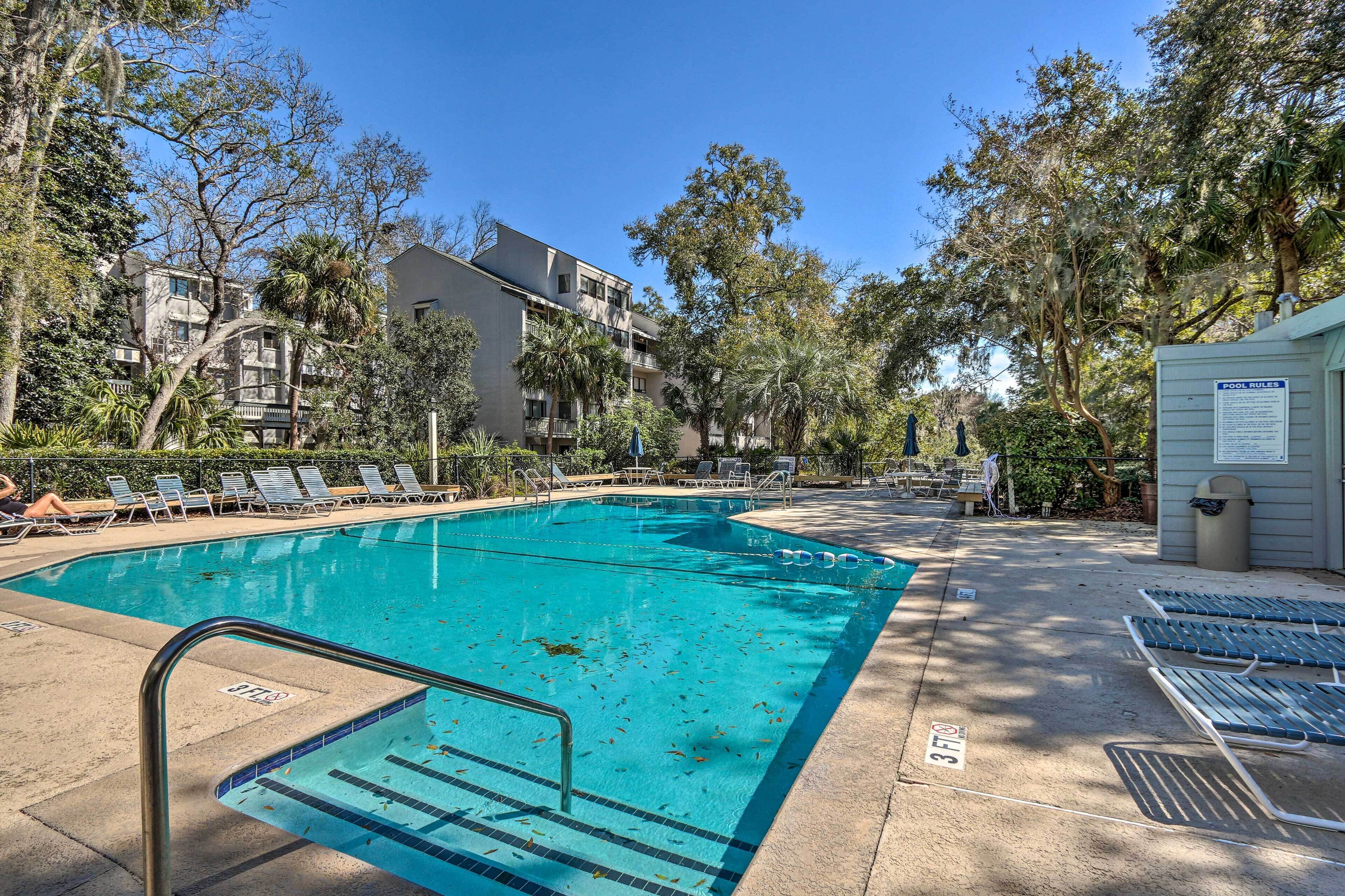 A swimming pool with lounge chairs, a pool rule sign, and surrounding trees.