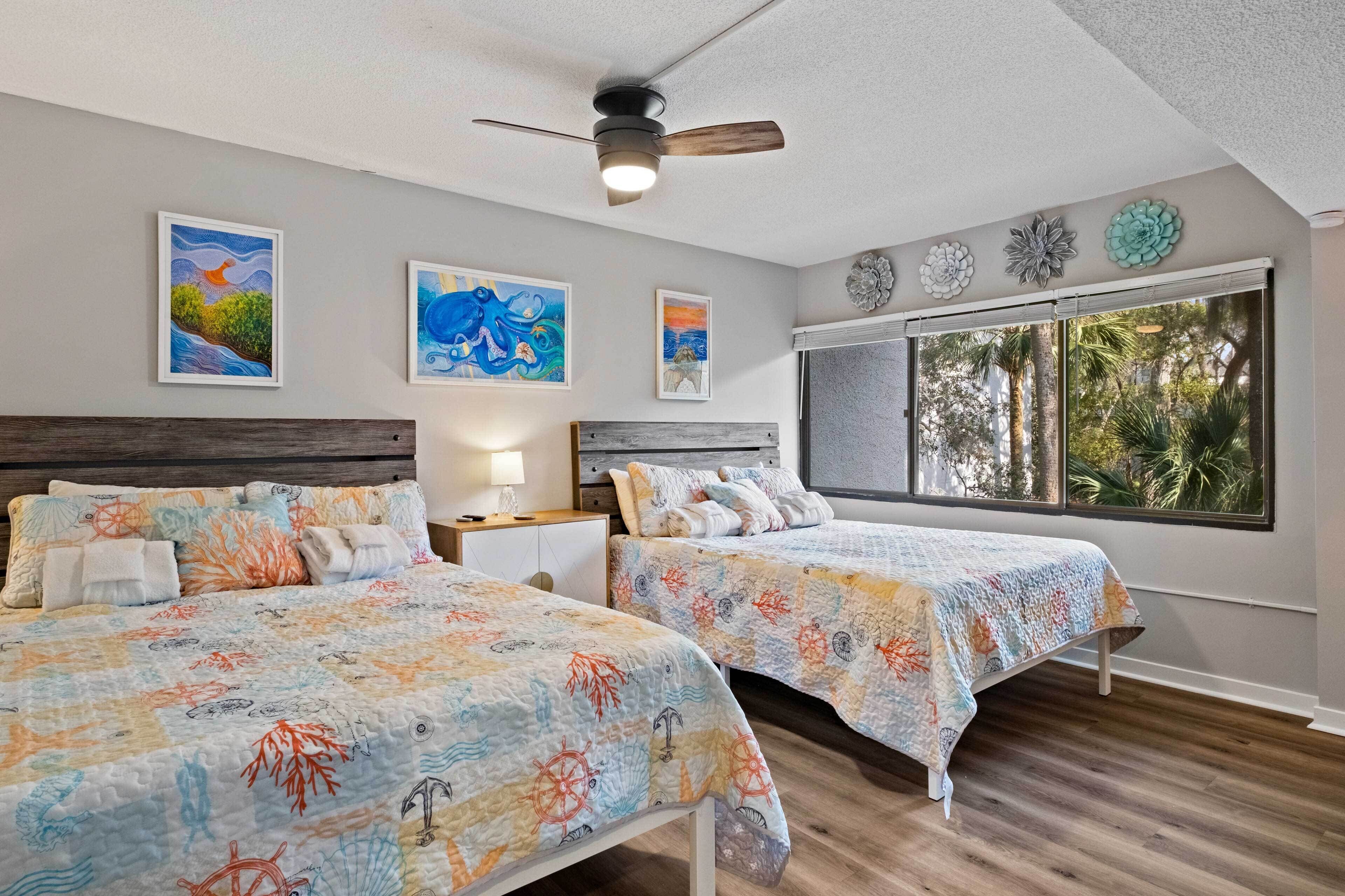 A bedroom with two beds, a ceiling fan, and artwork on the walls.