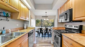 A modern kitchen with wooden cabinets, stainless steel appliances, and a dining area with a view of the outdoors. - Walk to Coligny Beach Park: Coastal Oasis w/ Pool (Hilton Head Island)