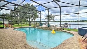 A covered swimming pool with a view of a lake, surrounded by a brick deck and outdoor furniture. - Florida Family Home w/ Dock on Saw Mill Lake! (Clermont)