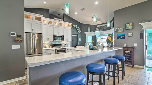 A modern kitchen with white cabinets, stainless steel appliances, and a large island with bar stools. - Florida Family Home w/ Dock on Saw Mill Lake! (Clermont)