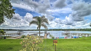 A lakeside view with a palm tree, dock, and a signpost with directions. - Florida Family Home w/ Dock on Saw Mill Lake! (Clermont)