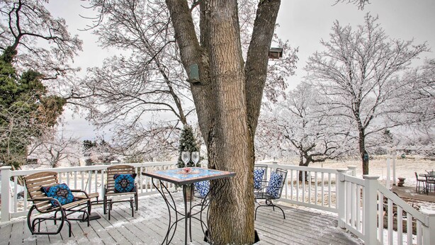 A wooden deck with a white railing, two chairs with patterned cushions, and a table with a glass top.