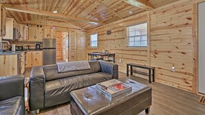 A cozy cabin interior with a wooden ceiling, a sofa, a dining table, and a kitchen area.