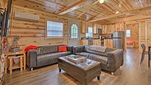 A cozy cabin interior with a large leather sectional sofa, a wooden dining table, and a kitchenette area.