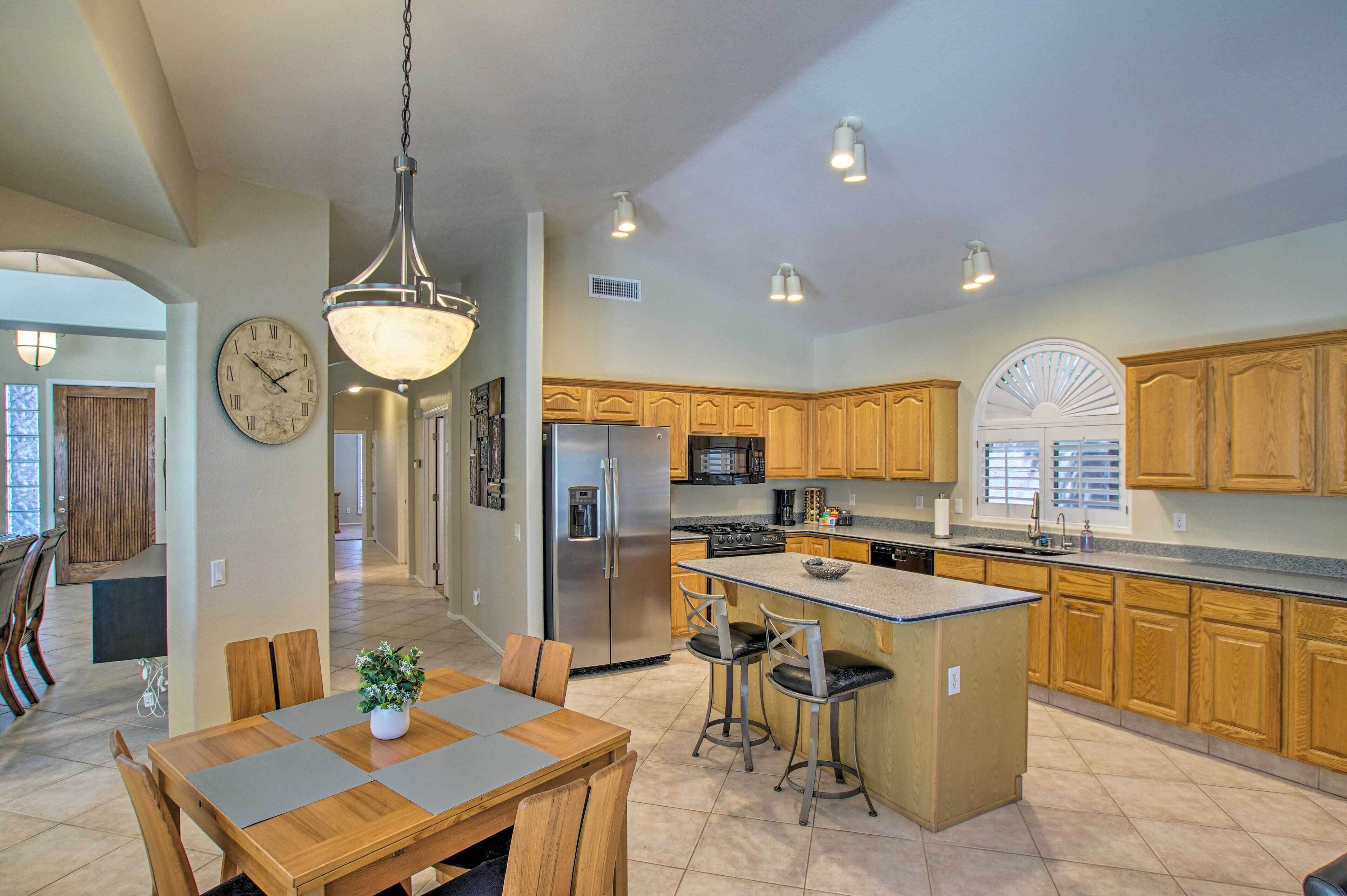 A spacious kitchen with wooden cabinets, a central island, stainless steel appliances, and pendant lighting.