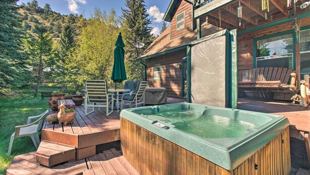 Eine Holzterrasse mit Whirlpool, Gartenmöbeln und Blick auf einen bewaldeten Hügel.