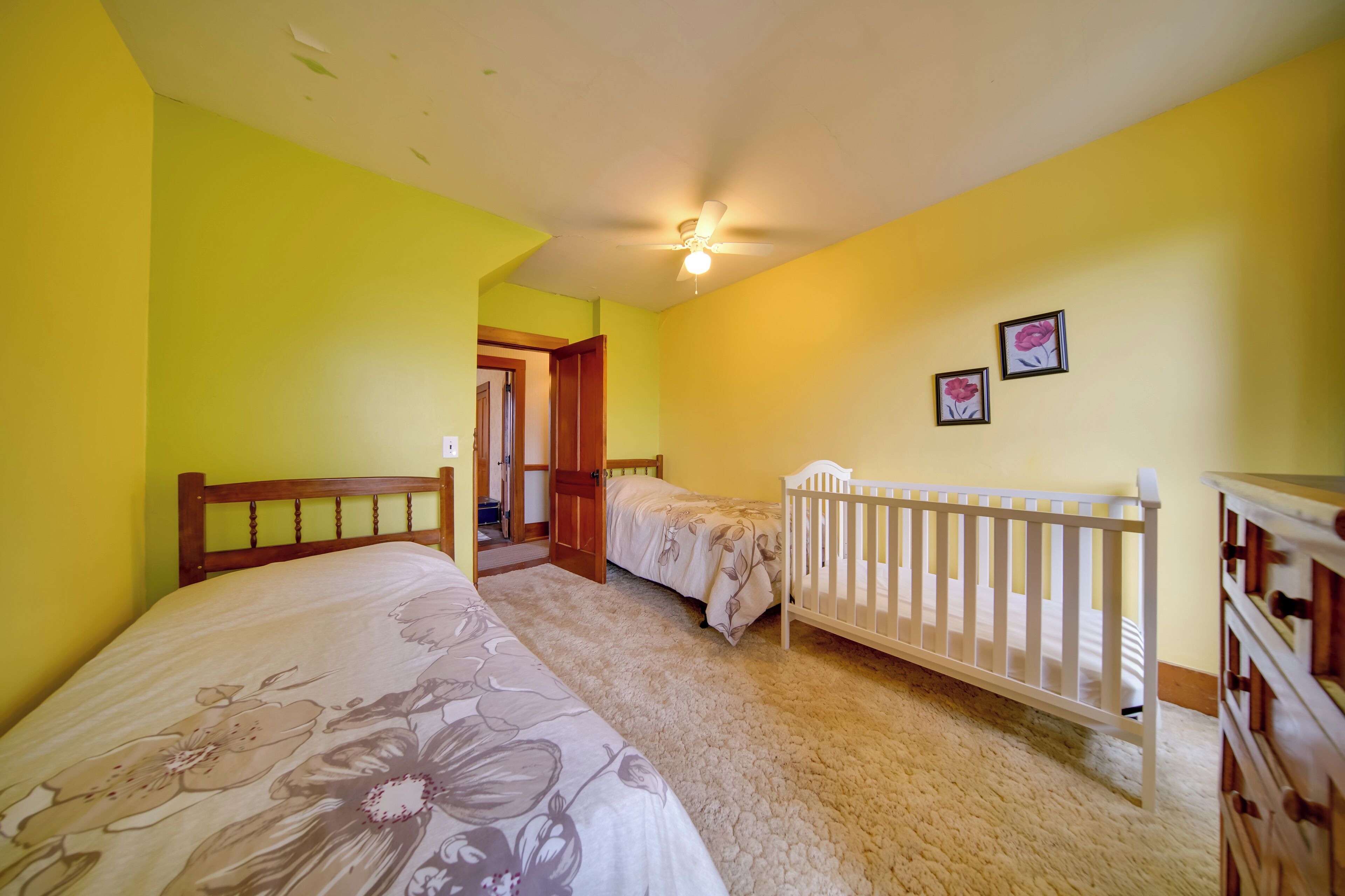 A bedroom with two beds, a crib, a ceiling fan, and a dresser.