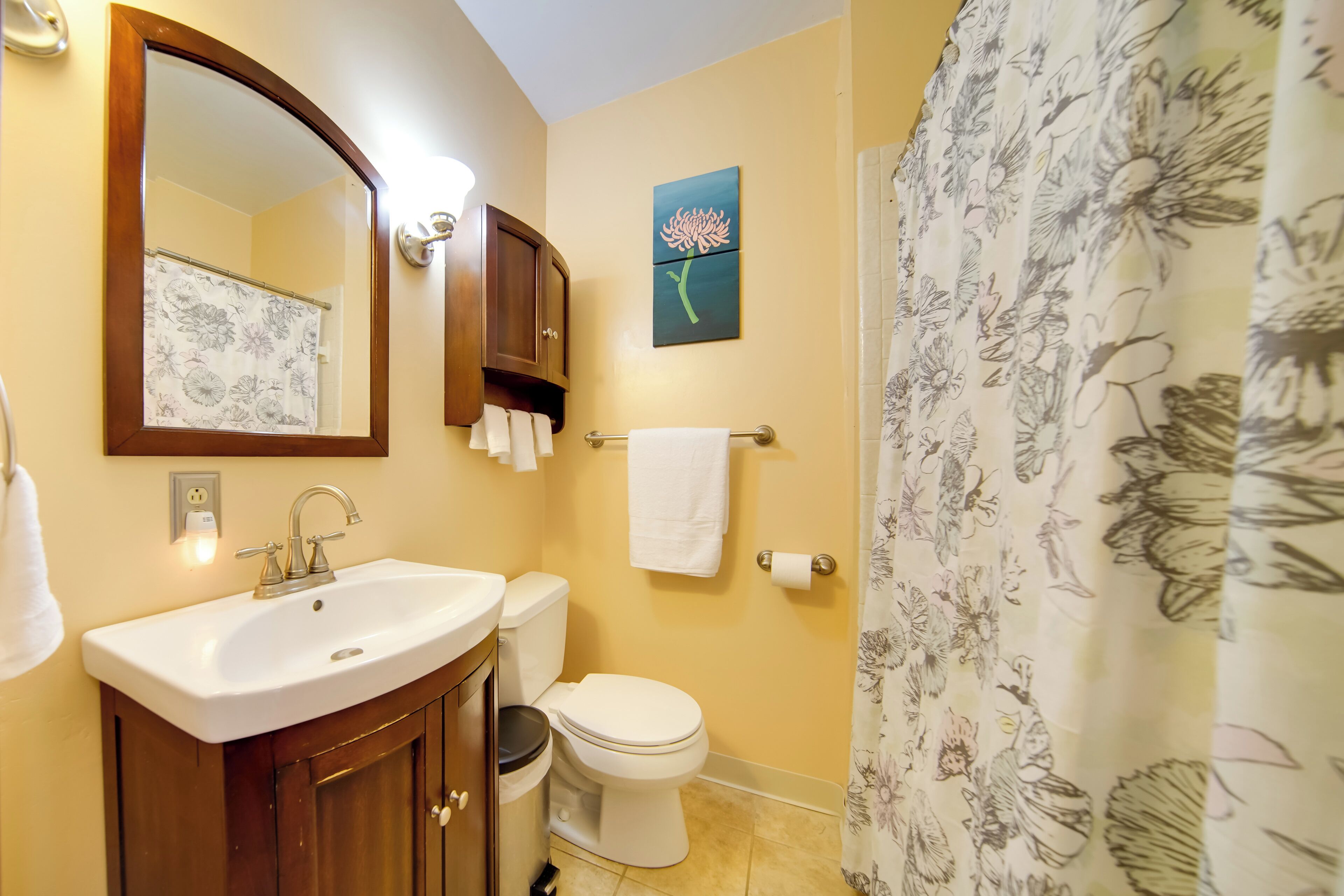 A bathroom with a sink, mirror, toilet, and shower curtain.