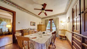 A dining room with a wooden table set for six, surrounded by wooden chairs. A ceiling fan is visible above the table. - Historic Victorian Farmhouse w/ Porch & Views! (Mayville)