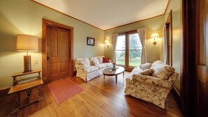 A cozy living room with two floral-patterned sofas, a wooden coffee table, a lamp, and a door. - Historic Victorian Farmhouse w/ Porch & Views! (Mayville)