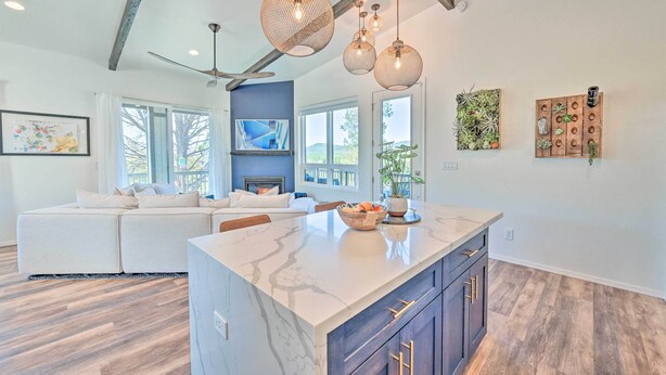 A spacious living area with a large white sofa, a marble island with dark cabinets, and a ceiling fan. - Mtn Views & Gas Fire Pit: Luxe Pine Escape! (Pine)