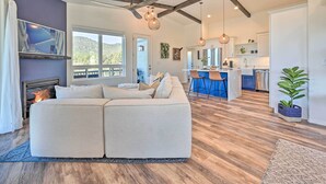 A modern living room with a sectional sofa, a fireplace, wooden flooring, and a view of the kitchen and outdoors. - Mtn Views & Gas Fire Pit: Luxe Pine Escape! (Pine)