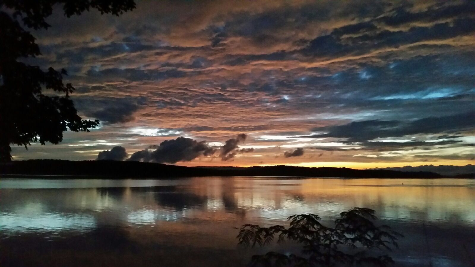 A calm lake reflecting a sunset sky with clouds.