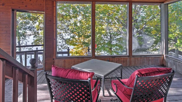Un espacio de estar al aire libre cubierto con una mesa, dos sillas, ventanas grandes y una terraza de madera.
