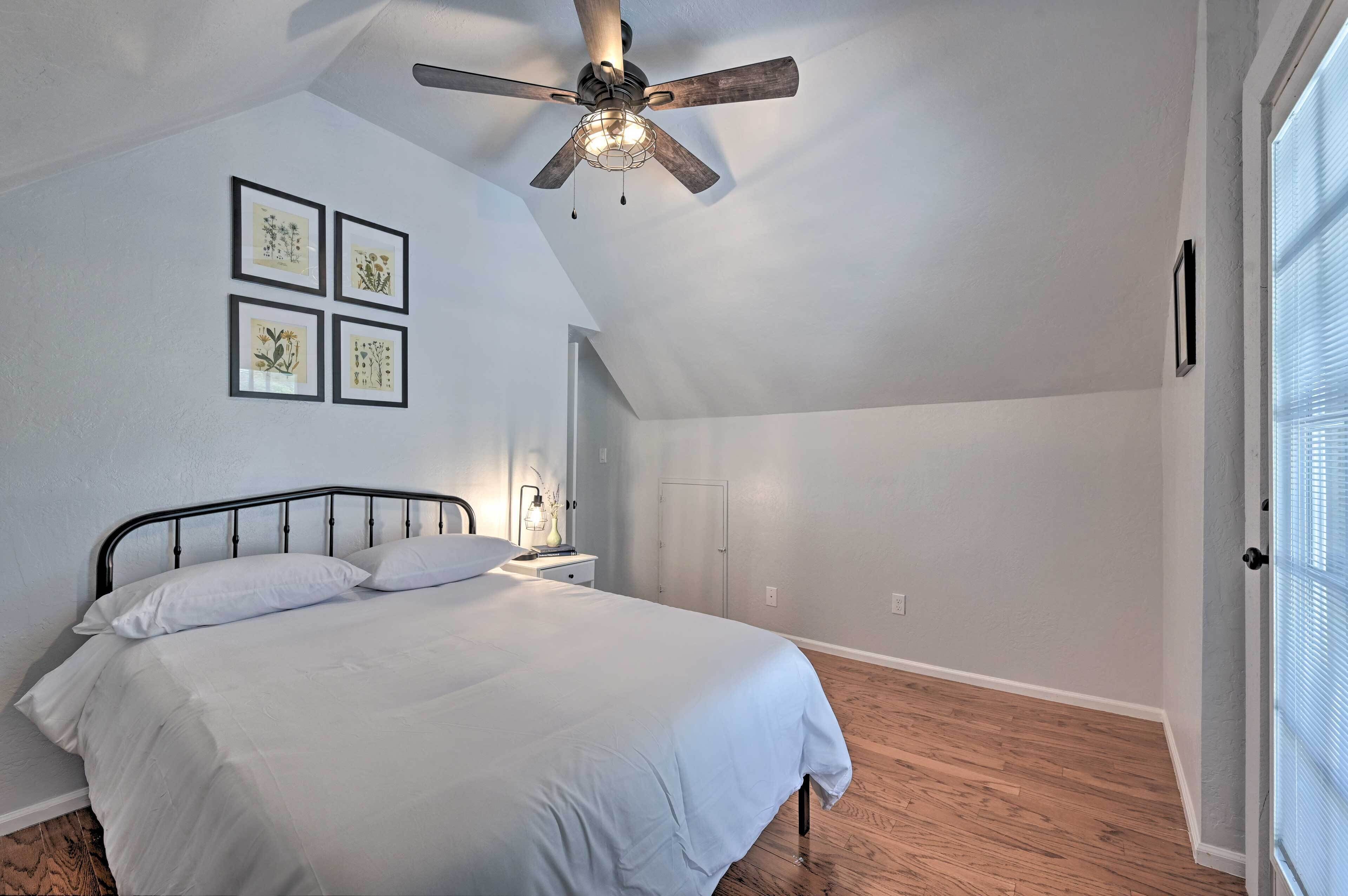 A bedroom with a bed, ceiling fan, framed pictures, and a door.