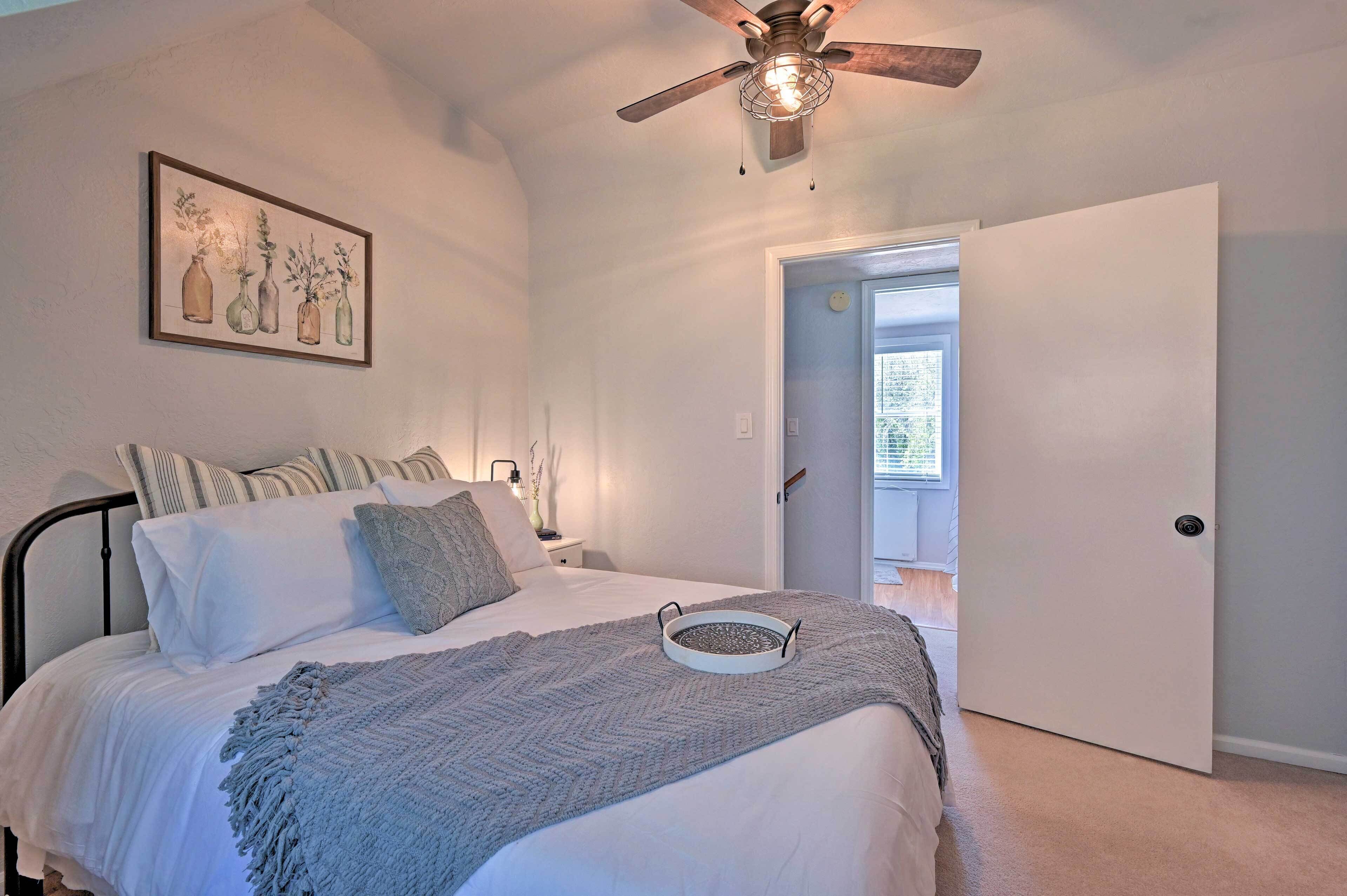 Un dormitorio con una cama, un ventilador de techo, una obra de arte enmarcada y una puerta que da a un balcón.