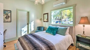 A bedroom with a large bed, a chandelier, an air conditioner, a window with a view, a chair, and a lamp. - Victorian Gem! Steps to Dine, Shop & Hike (Carbondale)
