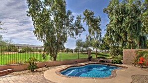 Piscina com um terraço de tijolos, rodeada por árvores e uma área cercada, com vista para um campo verde e montanhas.