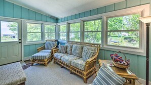 A room with a wicker sofa, two armchairs, a bench, and a table with a basket. - Breezy Silver Lake Getaway: Fishing Dock, Grill! (Mears)