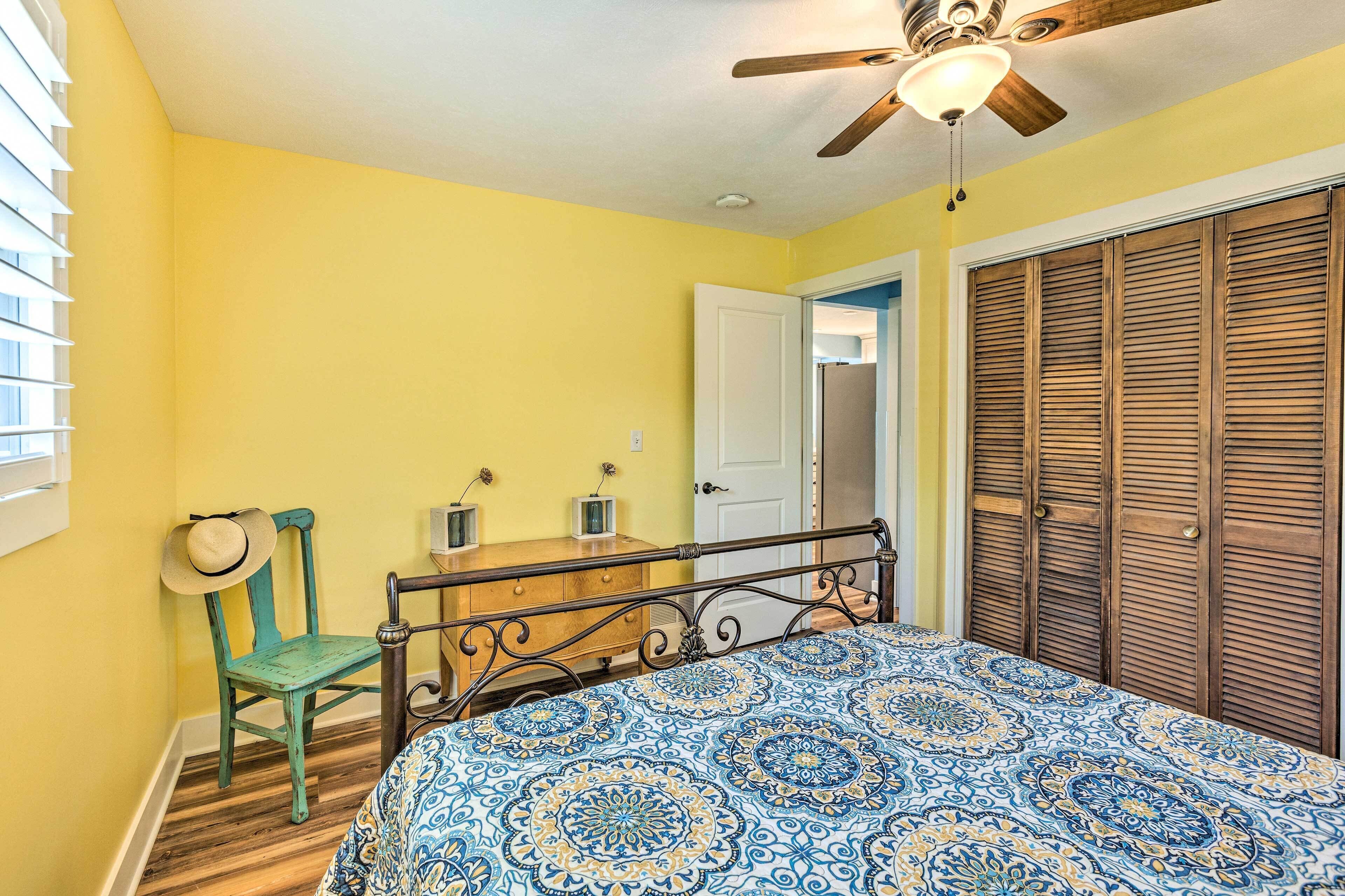 Une chambre à coucher avec un lit, une armoire en bois, une chaise verte, un ventilateur de plafond et une fenêtre avec des stores.