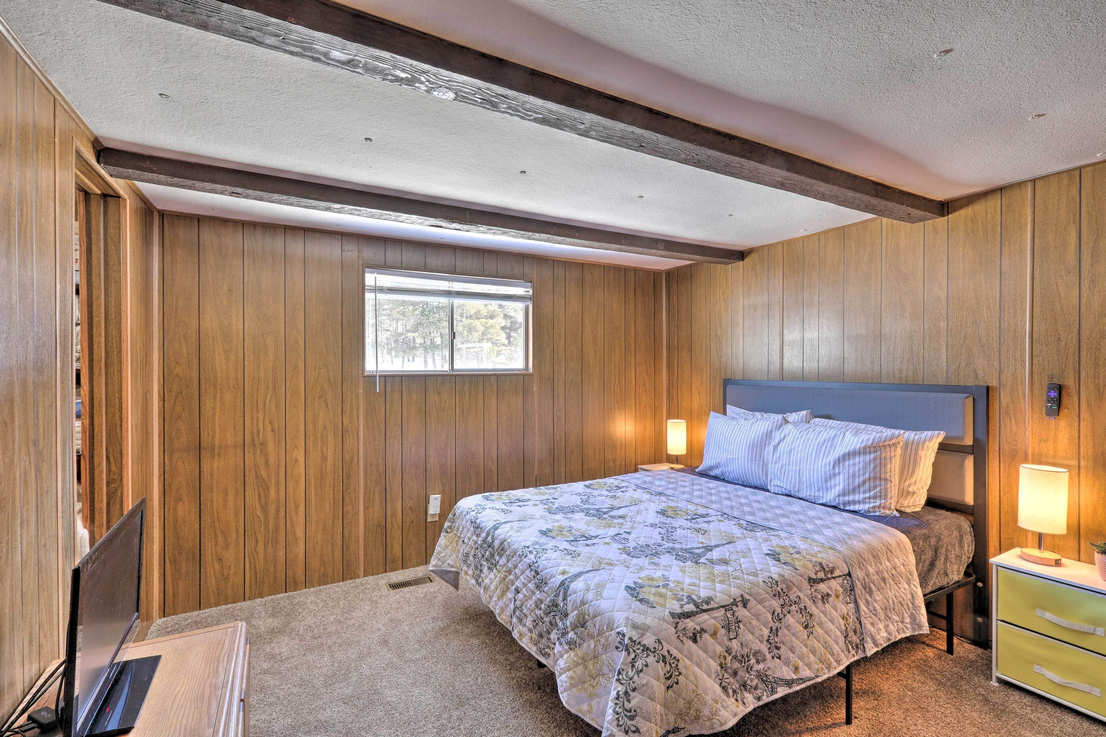 Une chambre avec un mur lambrissé en bois, un lit recouvert d’une courtepointe à motifs floraux, une lampe de chevet et un petit bureau avec un ordinateur portable.