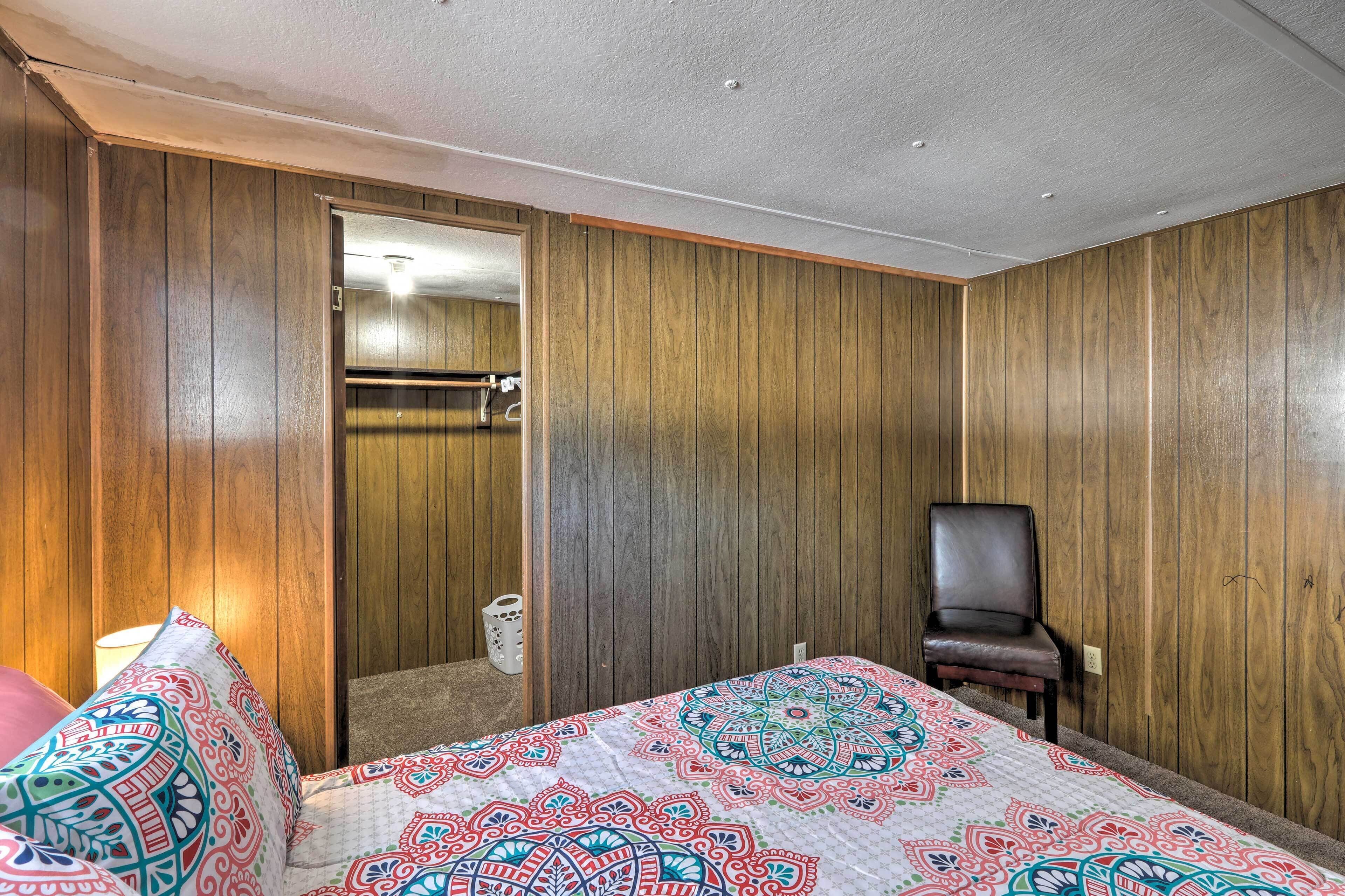 A hotel room with wooden panel walls, a bed with a colorful patterned bedspread, a chair, and a visible bathroom door.
