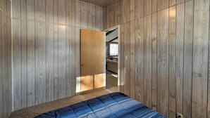 Une chambre avec des murs recouverts de panneaux de bois, un lit avec une couvre-lit à rayures bleues et une porte donnant sur une autre pièce.