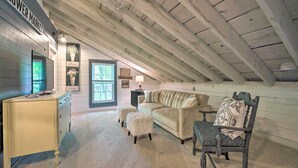 Une pièce mansardée chaleureuse avec un plafond en bois, un canapé beige, un fauteuil et un petit bureau.