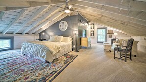Une chambre spacieuse située sous les combles, avec un grand lit, une chaise, un bureau et une horloge au mur.