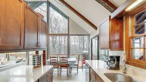 A kitchen with wooden cabinets, a large window, and a dining area with a table and chairs. - Breathtaking Brevard Home w/ Screened Porch! (Brevard)