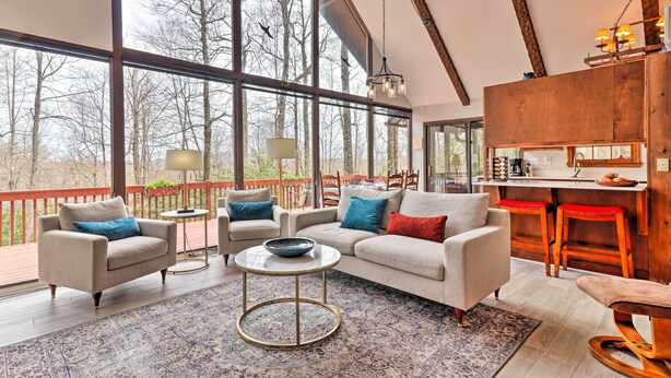 A spacious living area with large windows, a cozy seating arrangement, and a kitchen area. - Breathtaking Brevard Home w/ Screened Porch! (Brevard)