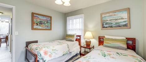 A bedroom with two wooden beds, floral bedding, a nightstand with a lamp, and two wall-mounted paintings.