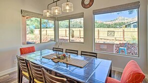 Un comedor con una mesa de vidrio, sillas y vista a un patio trasero con valla de madera.