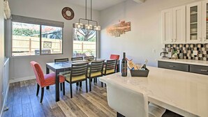 Una cocina moderna con armarios blancos, encimera de mármol y comedor con sillas de madera y una butaca tapizada en rojo.